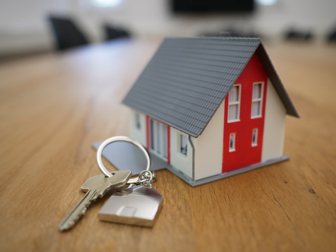 small house model with red and white paint next to house keys