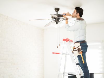 Attractive young technician stepping on a ladder and installing a ceiling fan