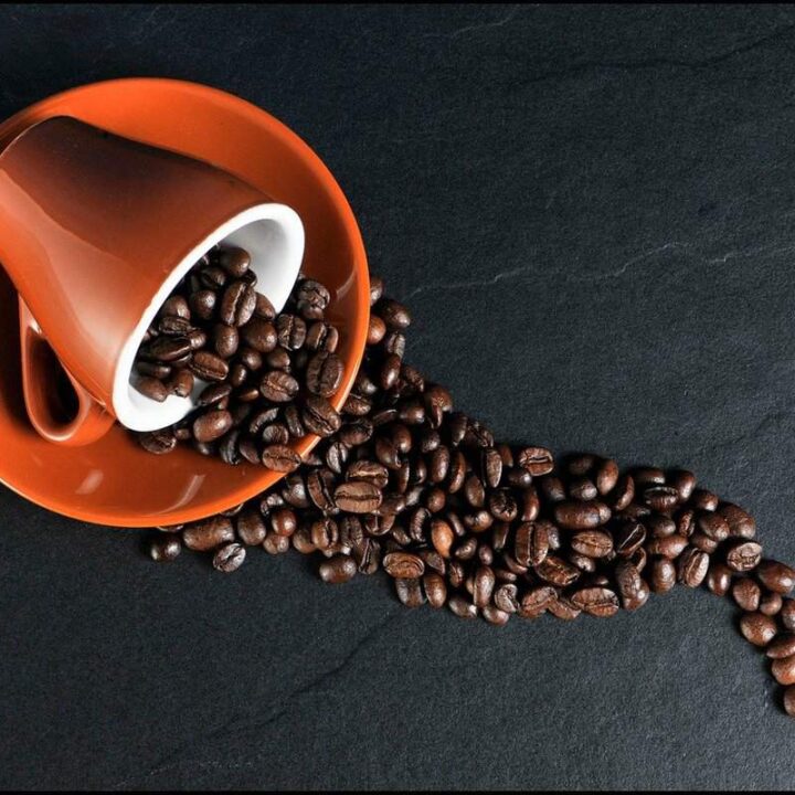burnt sienna colored coffee cup on side with coffee beans spilling out in neat design