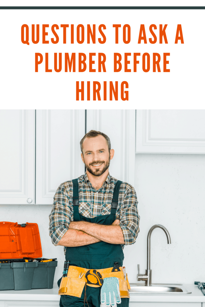 smiling handsome plumber standing with crossed arms and looking at camera in kitchen being asked questions before hiring