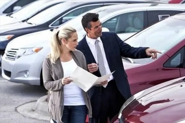 dealer walking car lot with woman interested in buying a pre-owned car