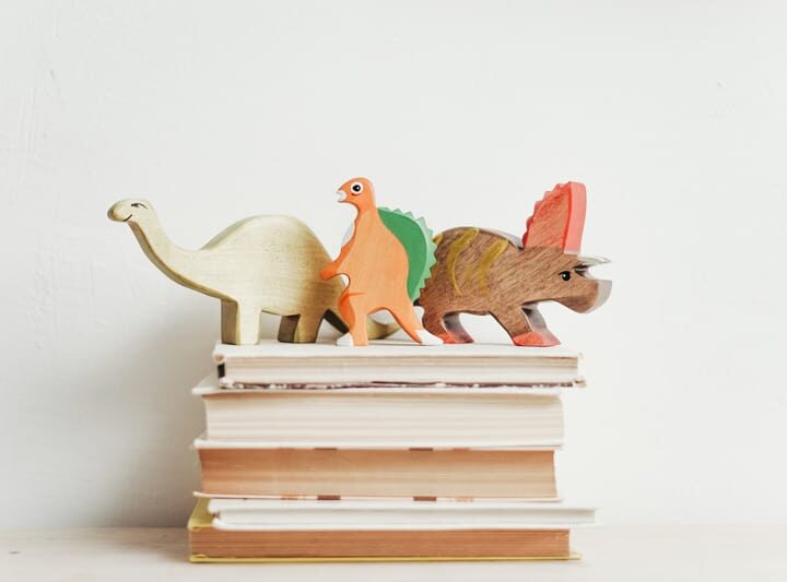 wooden dinosaurs on top of four dinosaur books you must read