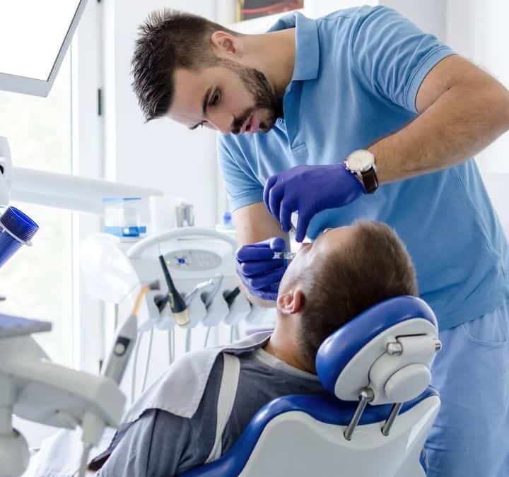 Image of male dentist in uniform giving anesthesia to male patient in stomatology office.