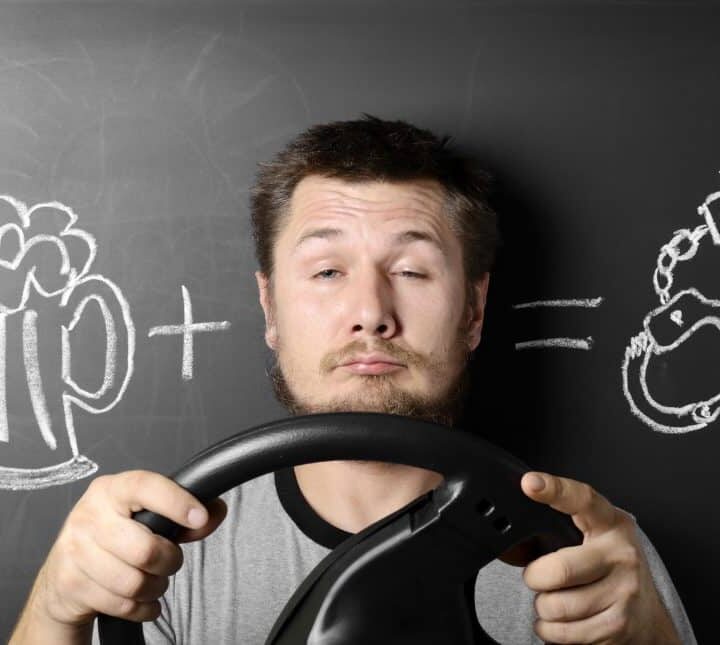Man against the chalkboard holding a steering wheel, drawing of a beer mug and handcuffs representing florida drivers drug and alcohol course