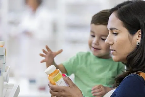 Mid adult woman reads medication dosage instructions on prescription medication. She is holding her toddler son.