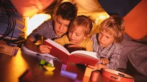 Cute siblings reading a story together under blankets at night