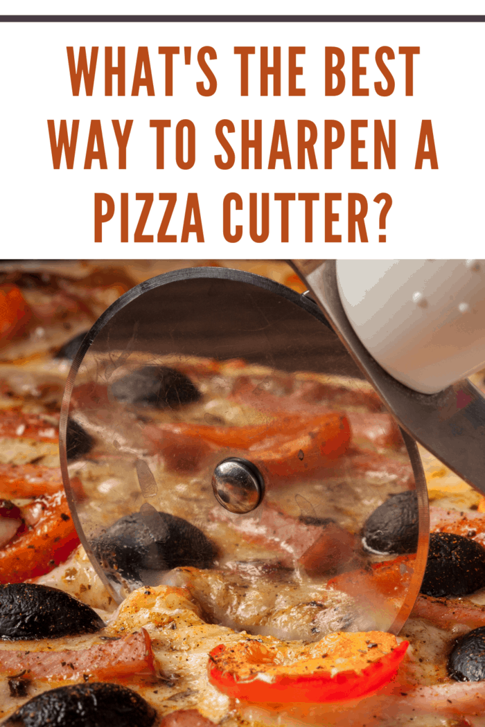 Letterbox panorama of pizza cutter (wheel) slicing ham pizza with capsicum and olives on wooden board on table