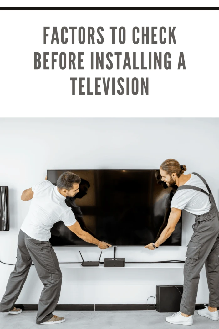 Two professional workmen in workwear installing a large TV monitor and audio system in the white living room. Home appliances installation concept