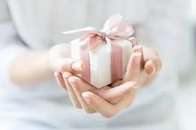 Close up shot of female hands holding a small gift wrapped with pink ribbon. Small gift in the hands of a woman indoor. Shallow depth of field with focus on the little box..