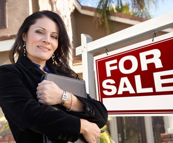Proud, Attractive Hispanic Female Agent In Front of For Sale Real Estate Sign and House