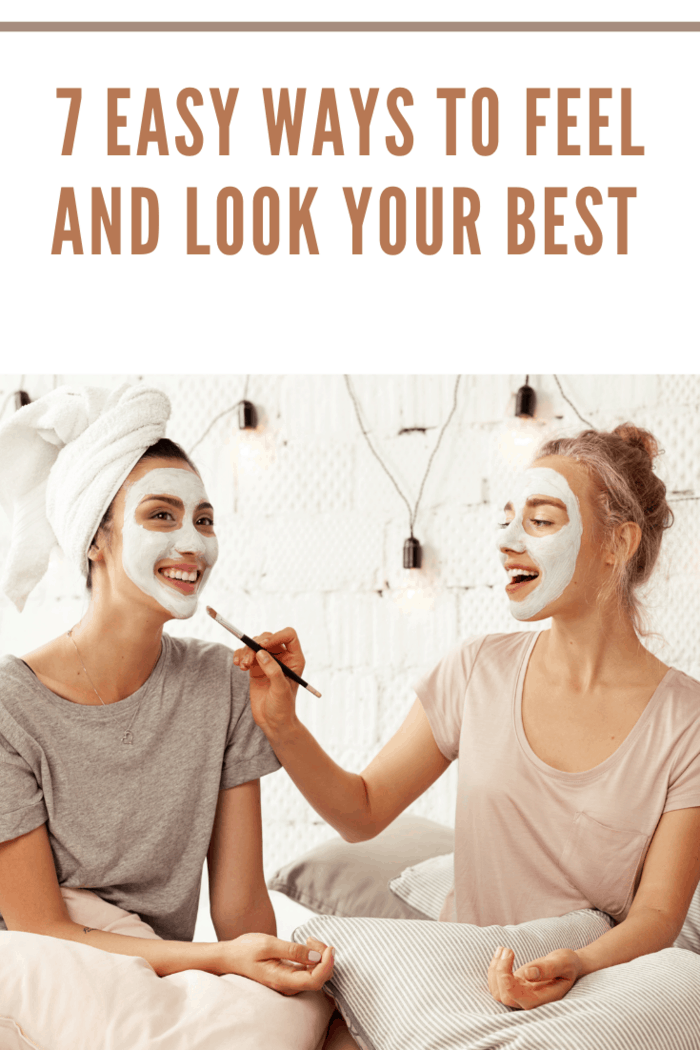 Portrait of attractive happy girls having fun sitting in bed with pillows. Cheerful women wearing facial cosmetic mask for soft smooth silk skin. Beauty skincare concept