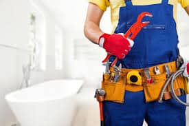 plumber with tool belt and wrench in hand standing in bathroom