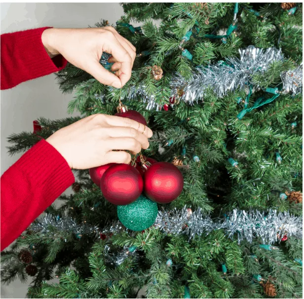 Female hands gathering red and green ornaments to be put into storage with Christmas tree in background
