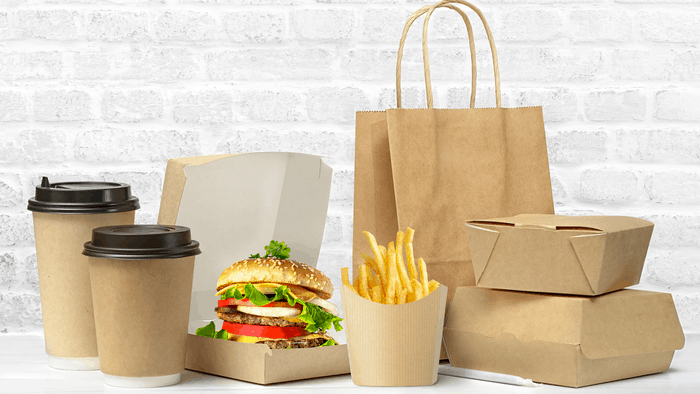Brown box with sandwich. Fast food packaging. Paper coffee cups, brown paper bag on the table on white brick wall background