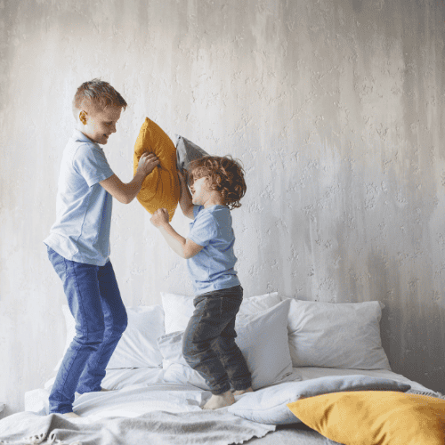 Full length side view outgoing boy playing with cheerful little brother with cushions. Happy boys having fun concept