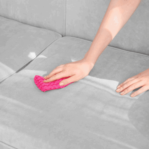 Person Cleaning Couch with Duster at Home