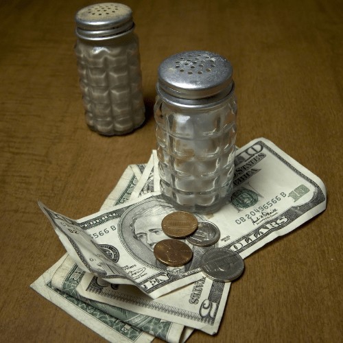 Salt and pepper shaker on a wood table. Salt shaker on money.