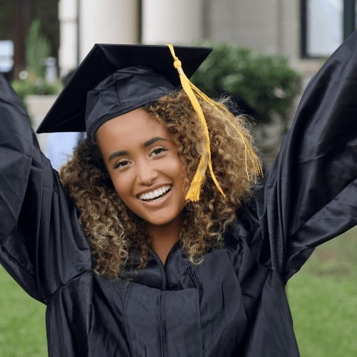 Smiling female college graduate raises up her arms and cheers after graduation ceremony.