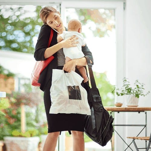 Shot of a busy businesswoman carrying a shopping bag and her baby while talking on the phone on her return from work