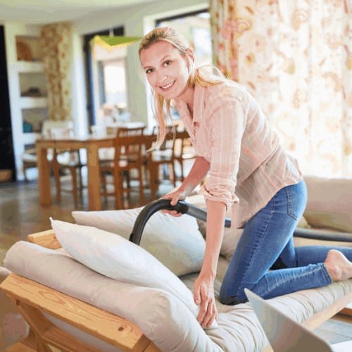 Housewife as a cleaning lady during spring cleaning while vacuuming a sofa