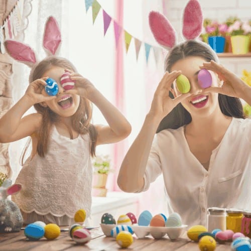 Mother and her daughter painting eggs. Happy family preparing for Easter. Cute little child girl wearing bunny ears.