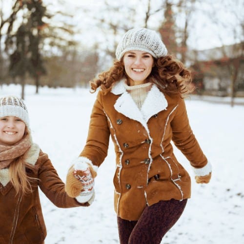 happy stylish mother and daughter in a knitted hats and sheepskin coats with mittens in a knitted hat and sheepskin coat outside in the city park in winter.