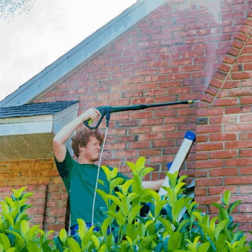 A young man cleans a red brick house exterior.