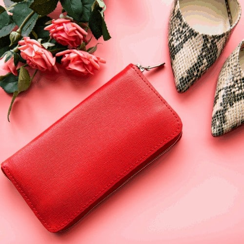 Red leather women wallet, roses and high shoes on pink background