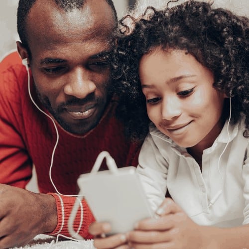 Content father and daughter listening to the music on smartphone while lying on the soft floor