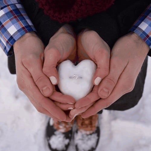 engagement ring in heart shaped snowball being held by couple