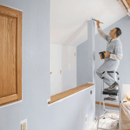Professional painter painting room with gray paint.