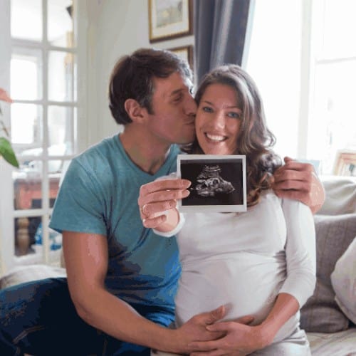 A couple are sat down showing their baby scan pictures.