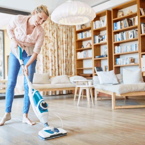Woman cleans floor with steam cleaner in the living room at home