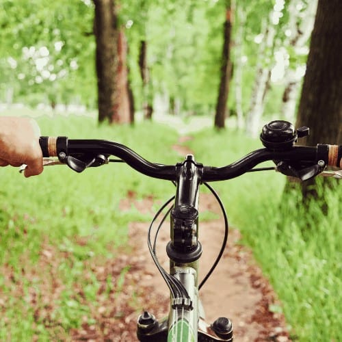 Close-up image of cyclist man hands on handlebar riding mountain bike on trail in summer park, face is not visible