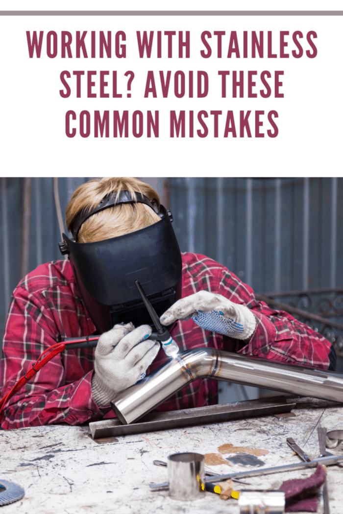 Young guy welder in a checkered red shirt welds a stainless steel pipe using agronomic welding to protect his eyes with a mask in an iron workshop. Modern welding methods.