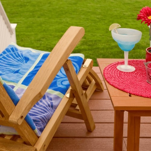 summer home scene, an outdoor deck or patio with wooden recliner and table, green grass in the background