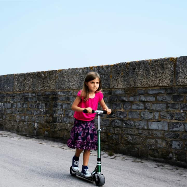 A girl rolls speedily down a hill on a scooter