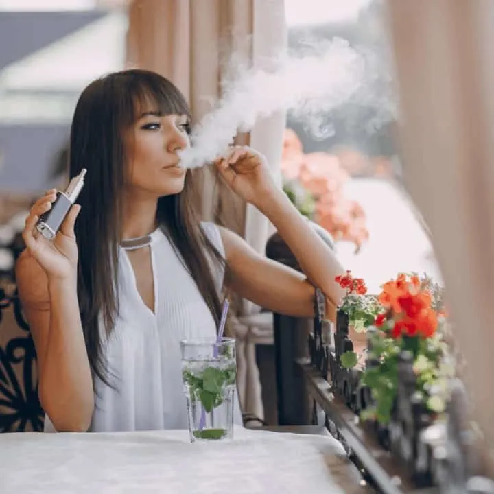 Beautiful brunette smoke electronic cigarette on the summer terrace of restaurant