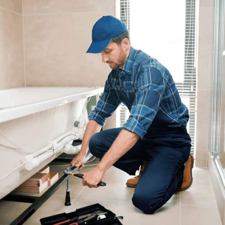 Young plumber or technician in workwear preparing detail for bathtub installation while sitting on squats