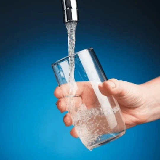 hand pouring a glass of water from water filter tap, blue background