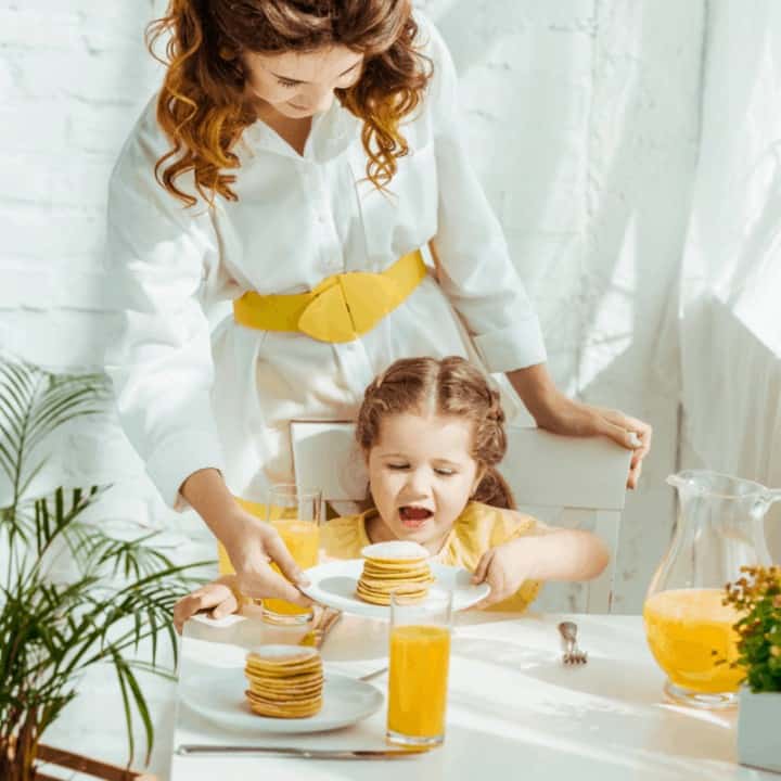 mother giving excited daughter pancakes for breakfast