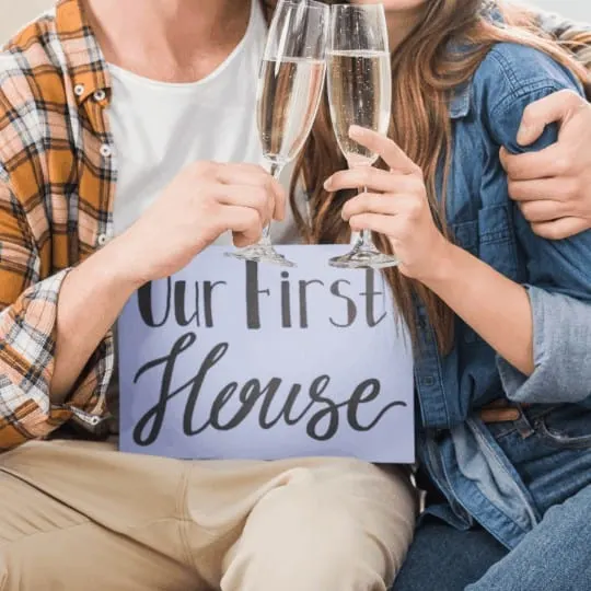 partial view of couple with our first house card clinking glasses of champagne, first home concept