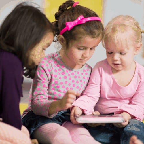 A multi-ethnic group of elementary age girls are playing together on a digital tablet.