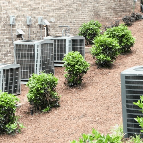 Multiple residential air conditioning units in a landscaped area of a home.