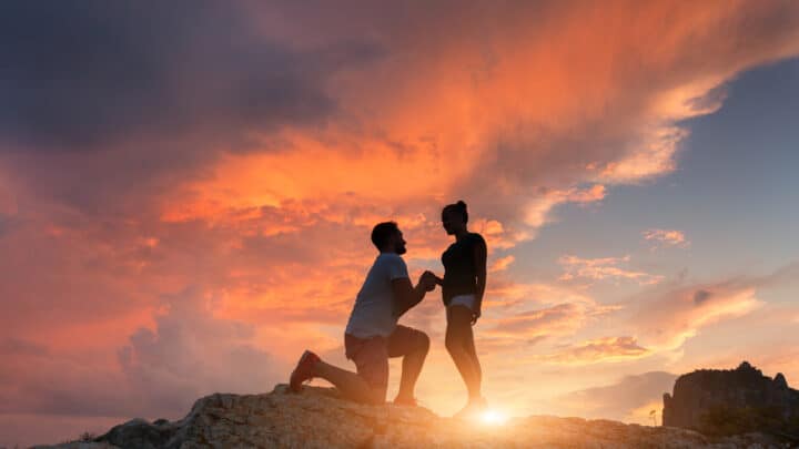Silhouette of a man proposing to his girlfriend at sunset.