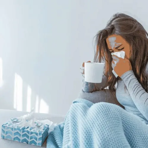 woman with cold under blanket blowing nose into kleenex