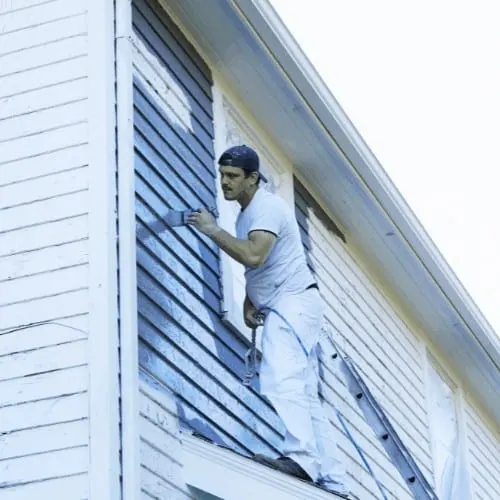 Man Brushing Paint On Exterior of Old Home