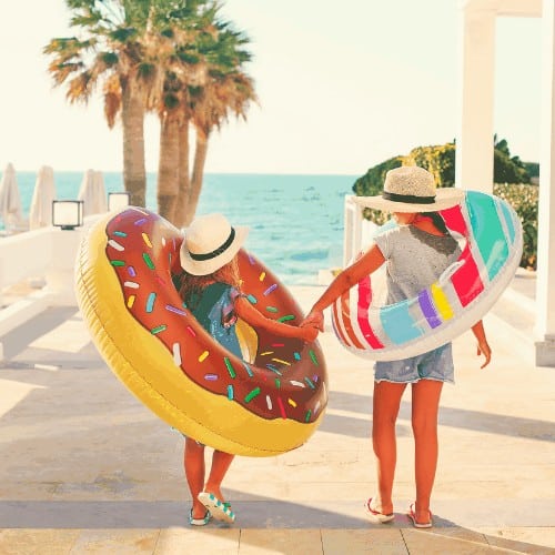 Two small girls with inflatable toys on the beach. Summer vacation and traveling concept
