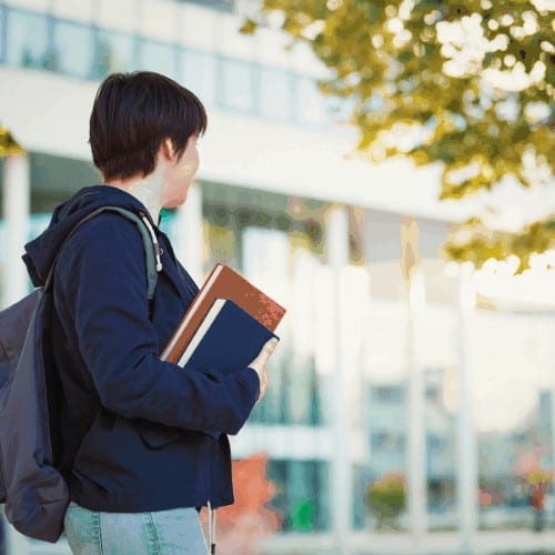 Side view outdoor autumn portrait of young student holding books looking to college.