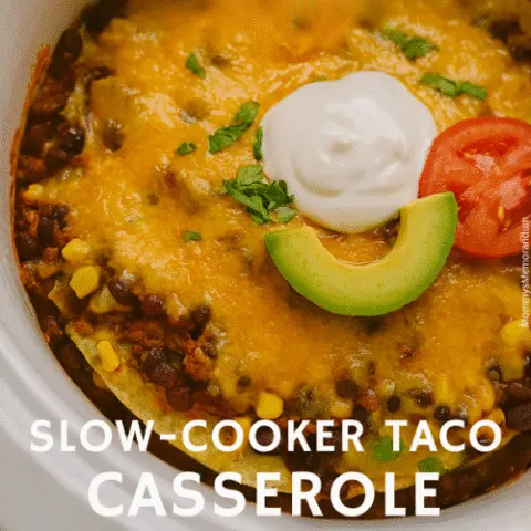 Overhead image of a Slow-Cooker Taco Casserole topped with sour cream, avocado, tomato, and cilantro, with overlay text that reads &ldquo;LET&rsquo;S &lsquo;SLOW&rsquo; DANCE &ndash; Slow-Cooker Taco Casserole.&rdquo; The dish is layered with tortillas, beef, beans, corn, and melted cheddar cheese in a white ceramic slow cooker.